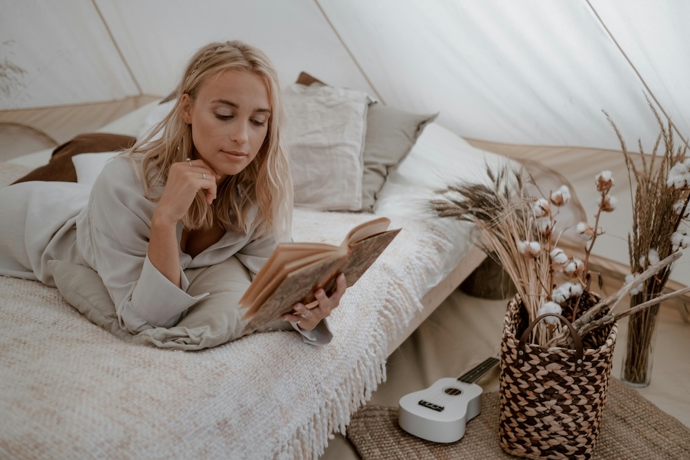 Woman lying on a bed reading inside a tent at a glamping destination.